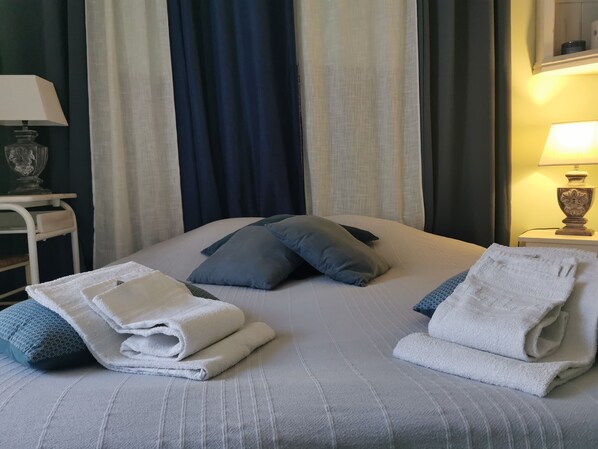 A neatly made bed with pillows, a folded towel, and a bedside lamp. - Les Tamaris (Campsegret)