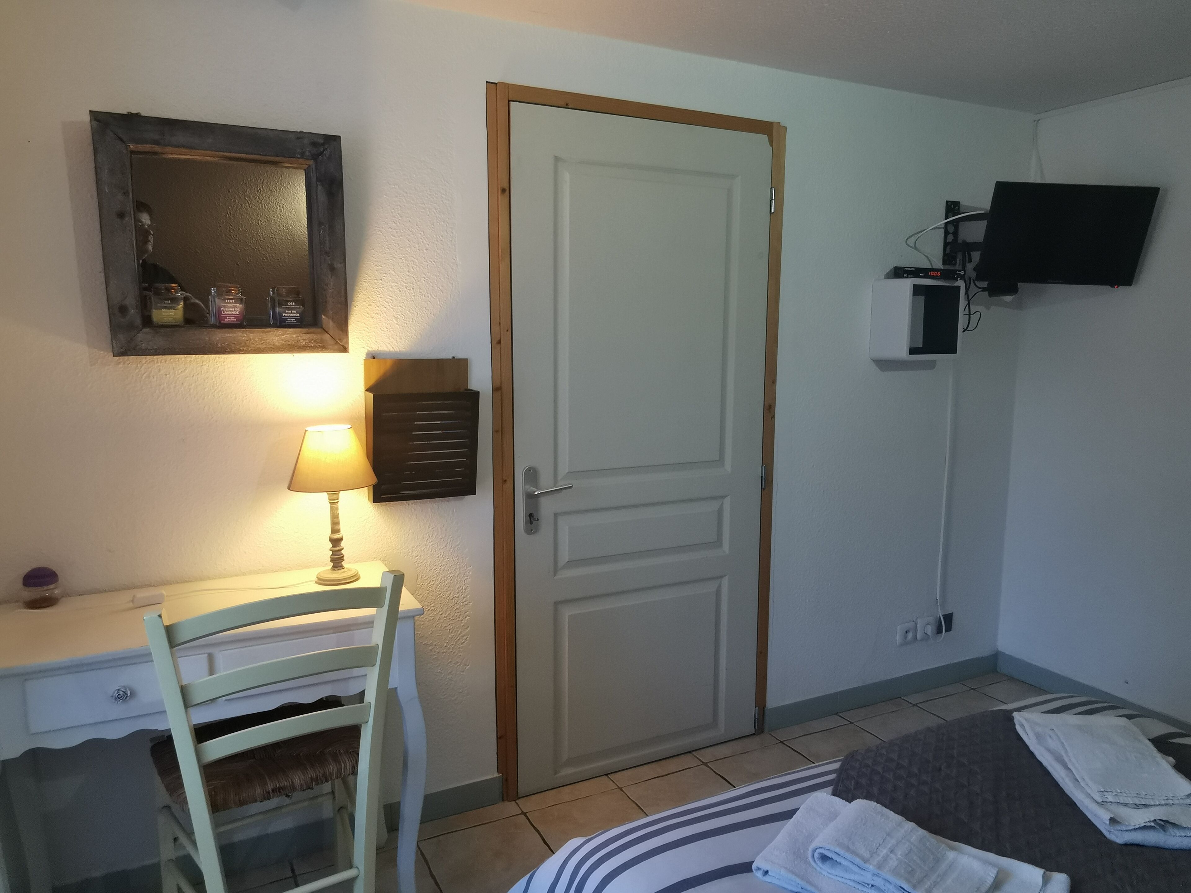 A room with a desk, chair, bed, TV, and a door.