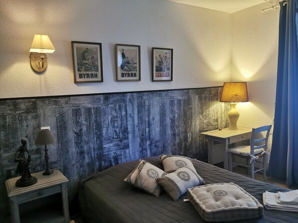 Habitación de hotel con cama, escritorio y silla. Tres cuadros enmarcados adornan la pared y hay una lámpara sobre el escritorio.