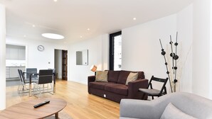 Ett modernt vardagsrum med en soffa, en grå fåtölj, ett träbord och en matplats med bord och stolar.