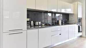 Ett modernt kök med vita skåp, rostfria vitvaror och ett stort fönster med utsikt över stadsbilden.