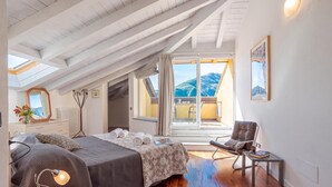 A bedroom with a sloped ceiling, a bed, a chair, and a view of mountains through a window.