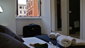 A hotel room with a bed, a suitcase, a bottle of champagne, and a window with a view of buildings. - Empire Suites (Rome)