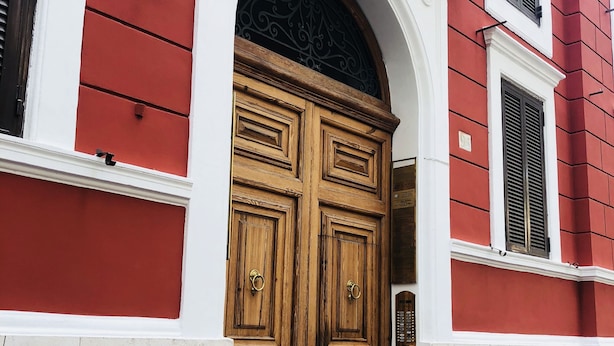 A red building with a large wooden double door, white trim, and a small window with shutters. - Empire Suites (Rome)