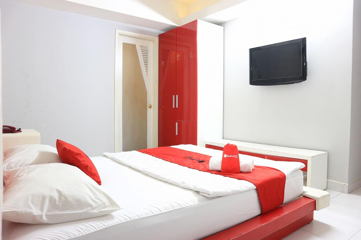 A modern bedroom with a bed, red and white bedding, a wardrobe, and a mounted TV.