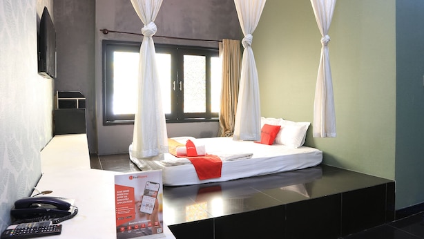 A hotel room with a bed, curtains, a bedside table with a remote control, and a brochure. - RedDoorz near Gia Dinh Church (Ho Chi Minh City)