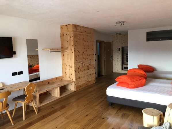 A modern room with a wooden desk, a bed with orange pillows, and a large mirror. - Pension Panorama Elisabeth (San Martino in Badia)