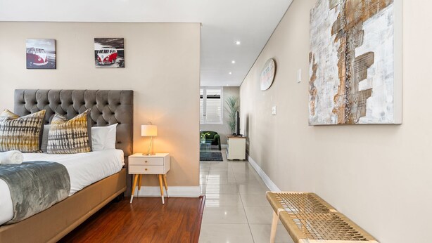 A modern bedroom with a bed, bedside table, lamp, and artwork on the walls. - Eden on the Bay 125 (Cape Town)