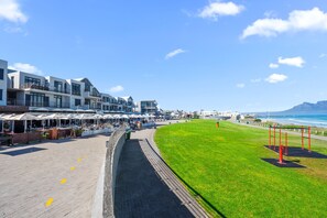 Un paseo marítimo costero con edificios modernos, una zona verde y vistas al océano.