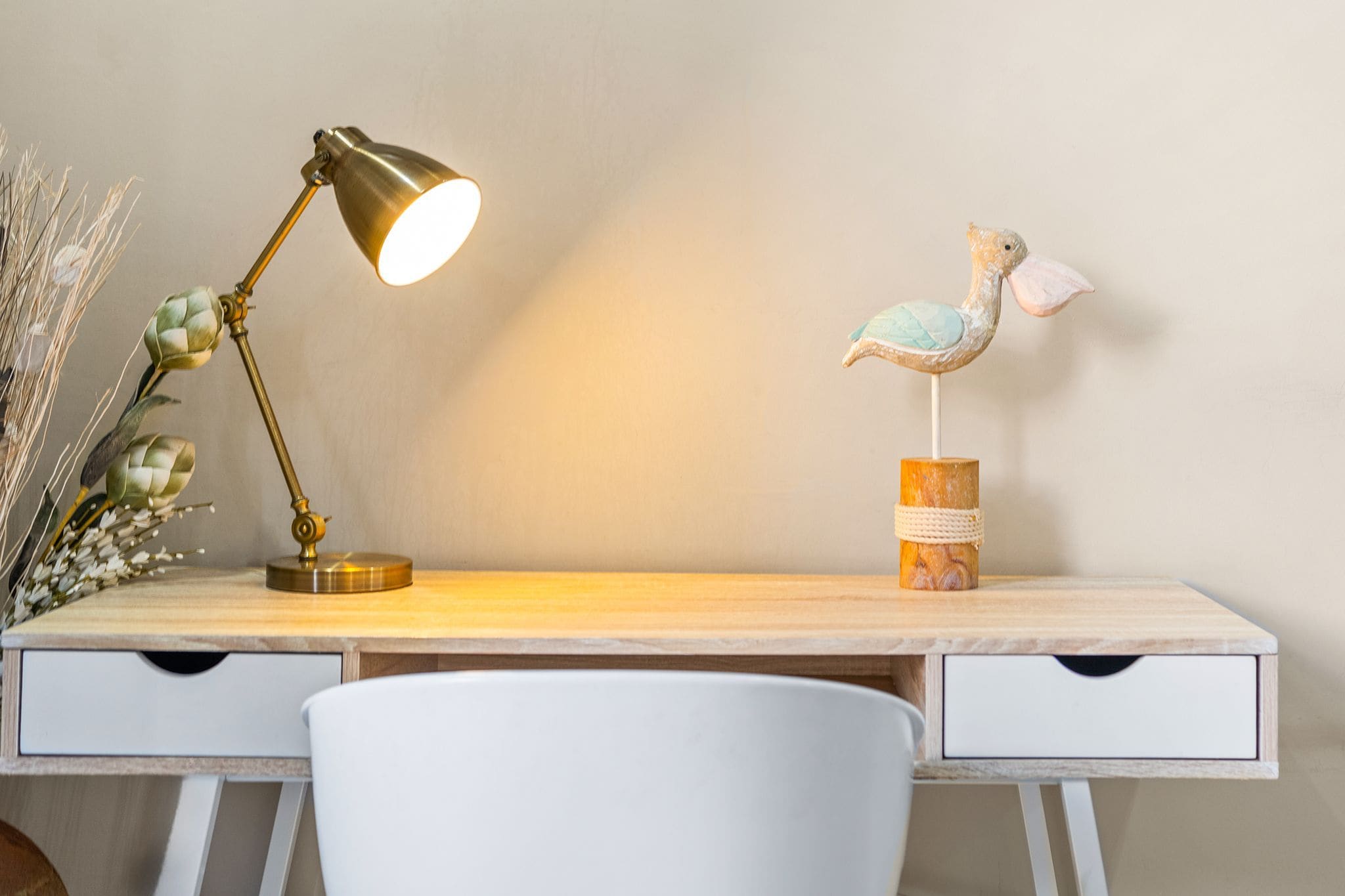 A desk with a lamp, a decorative bird, and a vase with dried plants.