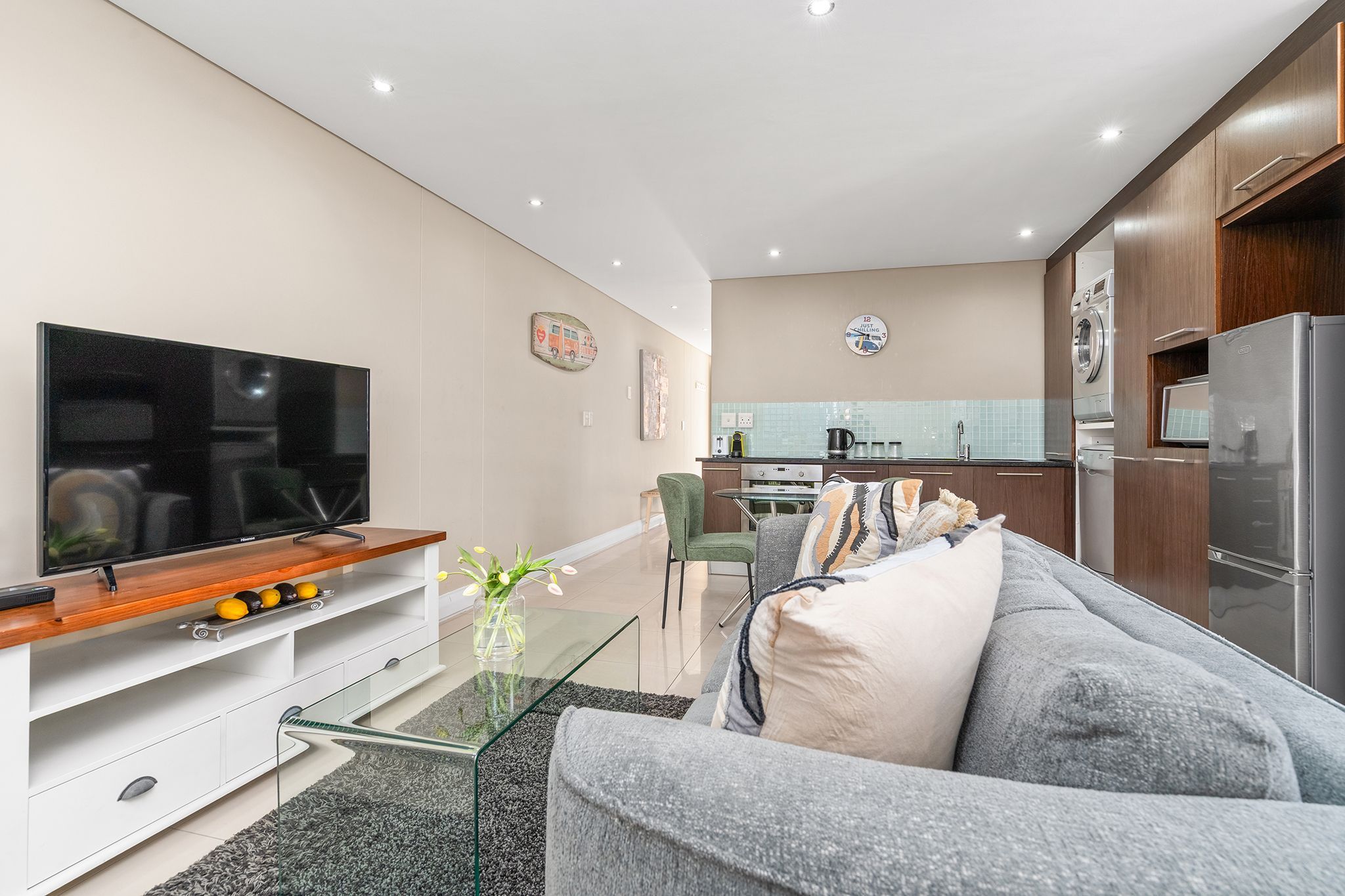 Una sala de estar moderna con un televisor de pantalla plana, una mesa de centro de vidrio y un sofá gris.