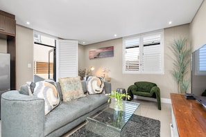 A modern living room with a grey sofa, a glass coffee table, and a green chair. - Eden on the Bay 125 (Cape Town)