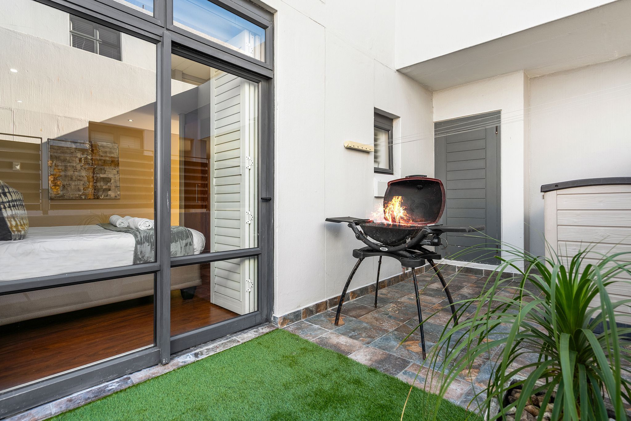 A modern outdoor patio with a barbecue grill, a bed with a view, and a small garden area.