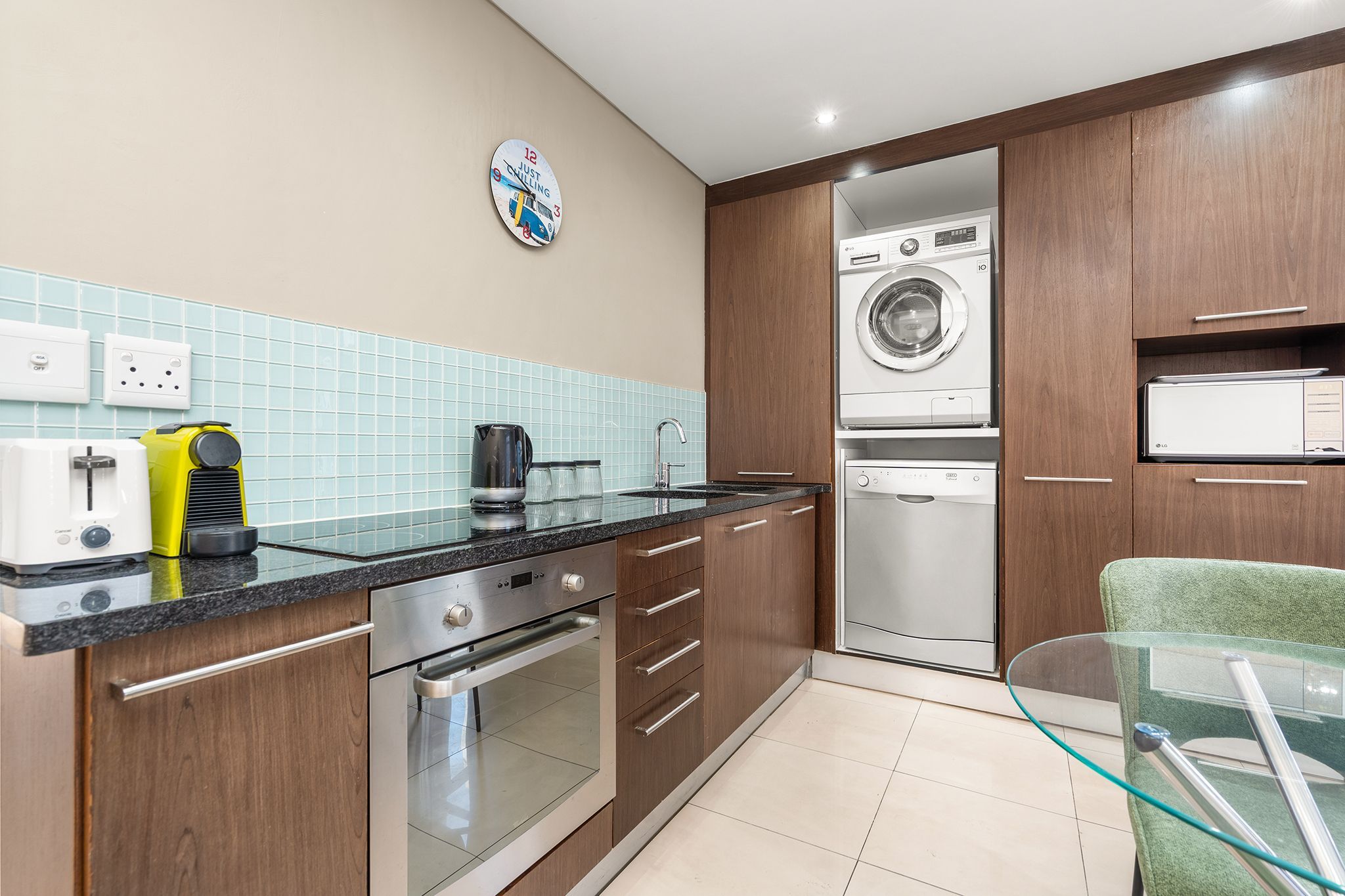 A modern kitchen with stainless steel appliances, a coffee maker, and a clock on the wall.