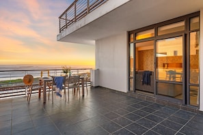 A balcony with a view of the sea, a dining table, and a sofa. - Eden on the Bay 167 (Cape Town)
