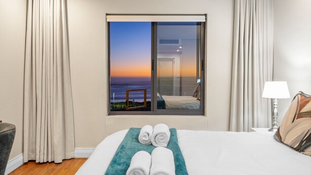 A hotel room with a bed, a view of the ocean, and a window with curtains. - Eden on the Bay 167 (Cape Town)