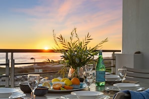 A table set for dining with a sunset view, a vase of flowers, and a bottle of Pilsener beer. - Eden on the Bay 167 (Cape Town)