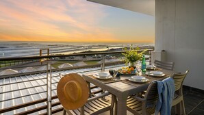 A balcony with a table set for two, overlooking a coastal landscape. - Eden on the Bay 167 (Cape Town)