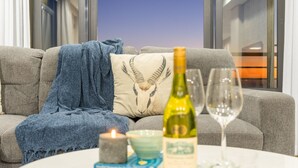 A cozy living room with a sofa, a blanket, a candle, a wine bottle, and a glass on a table. - Eden on the Bay 167 (Cape Town)