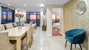 A modern living room with a dining area, large windows with a view, and a patterned wall. - Eden on the Bay 167 (Cape Town)