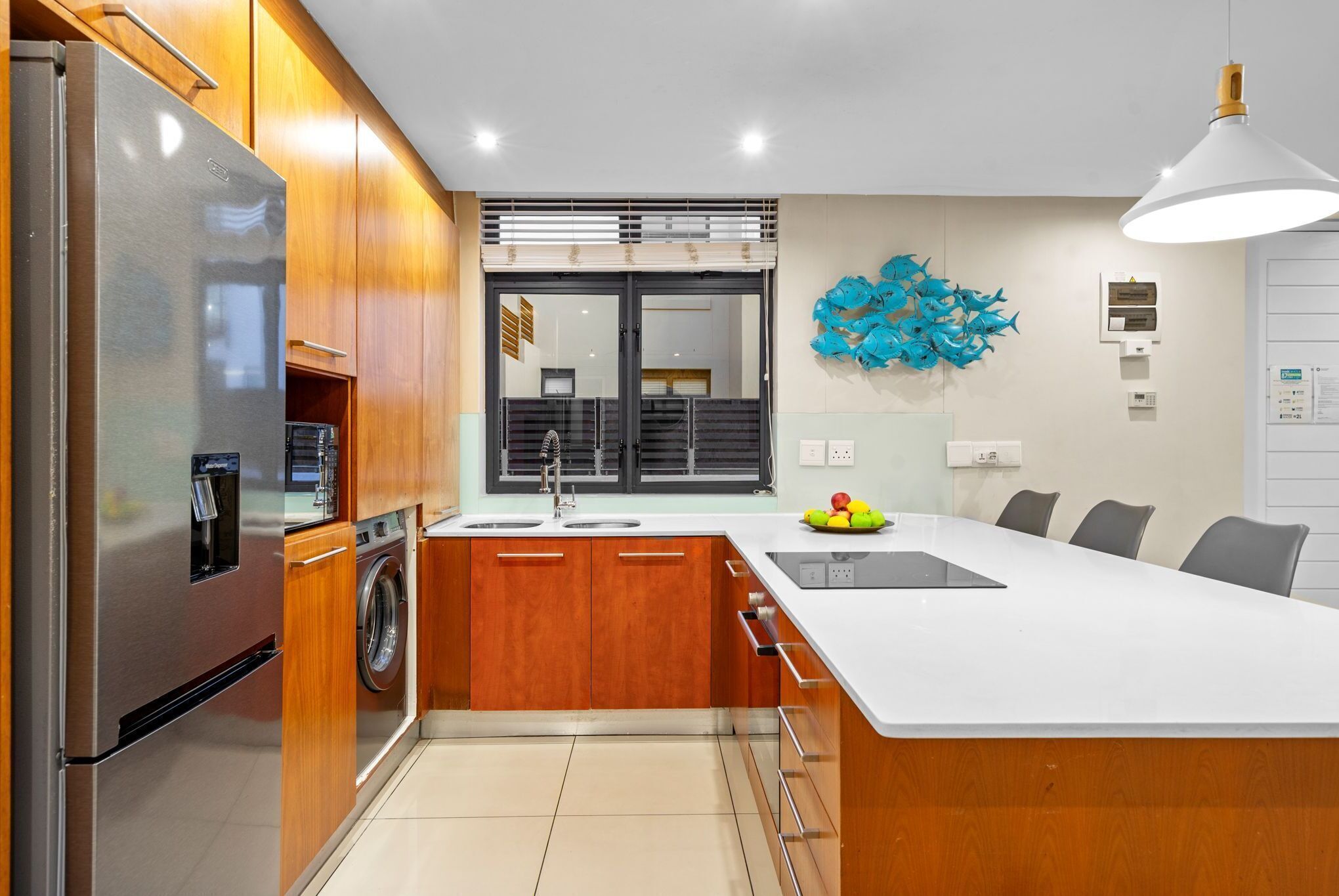 Una cocina moderna con un refrigerador de acero inoxidable, armarios de madera, lavadora integrada, una isla grande con pileta y una obra de arte abstracta azul en la pared.