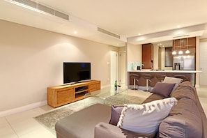 Ein modernes Wohnzimmer mit einem Flachbildfernseher, einer Holz-Unterhaltungsecke, einem braunen Sofa und einem Glastisch.