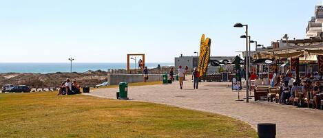 A coastal walkway with outdoor seating, a view of the sea, and a distinctive yellow structure.