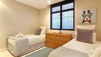 A bedroom with two beds, a wooden dresser, and a window with blinds.