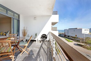 Uma varanda com mesa e cadeiras de madeira, churrasqueira e vista para o mar.
