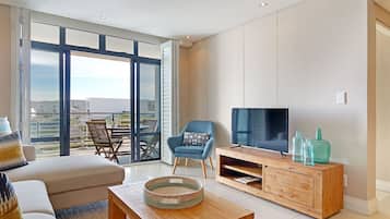 A spacious living room with a large window, a sofa, a coffee table, a TV, and a wooden entertainment unit.