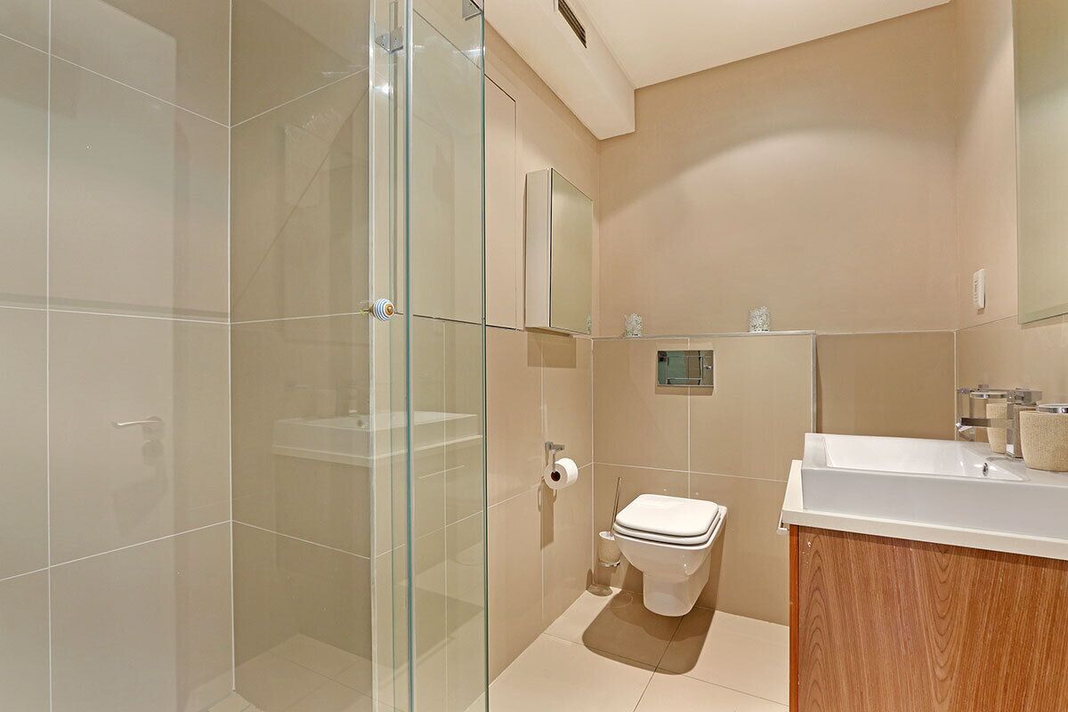A modern bathroom with a glass shower enclosure, a toilet, and a vanity with a mirror.