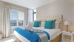 Une chambre avec un grand lit, une table de chevet, une fenêtre avec des rideaux et une vue sur la mer.