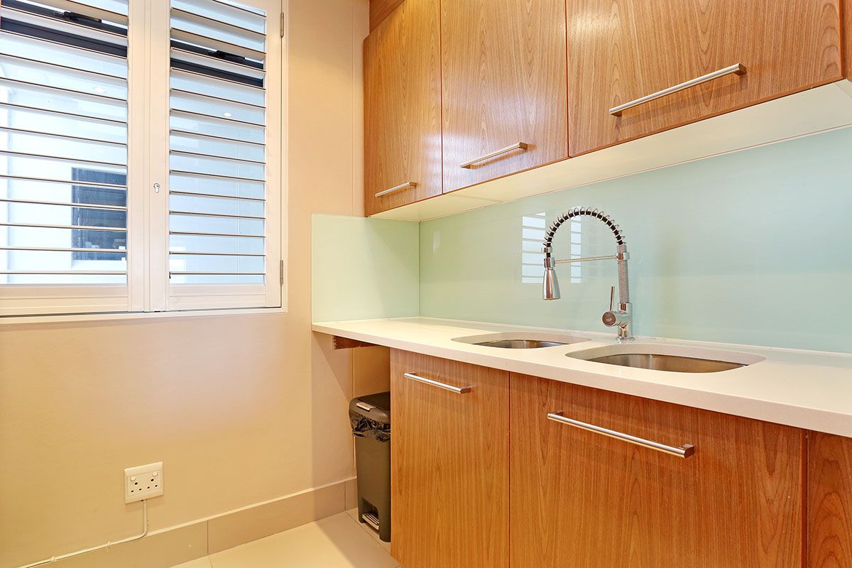 A kitchen with wooden cabinets, a white countertop, a double sink, and a window with blinds.