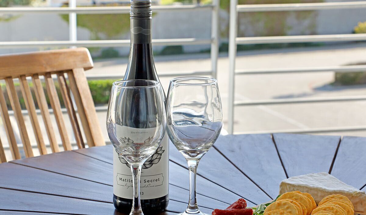 A bottle of wine, two glasses, and a cheese board with crackers on a wooden table.