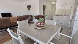 Un salon moderne avec un canapé blanc, une table à manger avec des chaises, un vase décoratif avec des plantes et un coin cuisine avec des meubles blancs et une décoration en forme de cœur sur le mur.