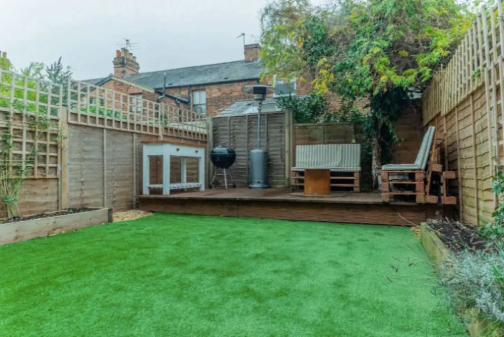 A backyard with a wooden deck, a barbecue grill, and a seating area.
