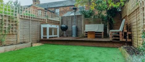 A backyard with a wooden deck, a barbecue grill, and a seating area.