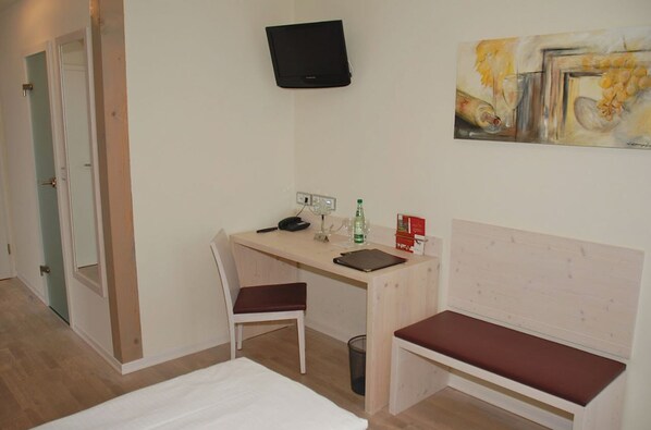 Habitación de hotel con escritorio de madera, una silla, cama, televisor montado en la pared y un cuadro en la pared.