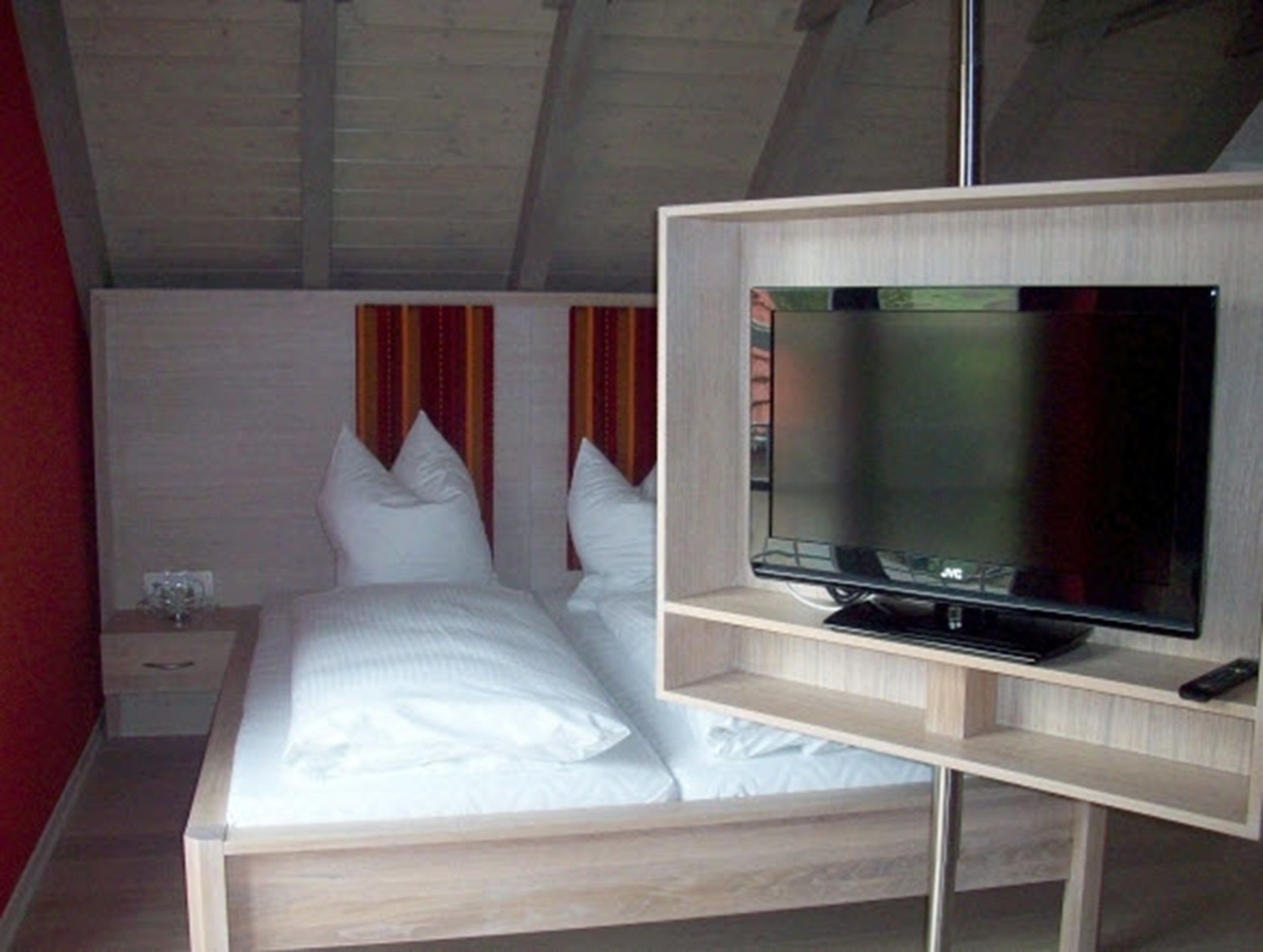 A bedroom with a bed, a TV on a stand, a nightstand, and a red wall.