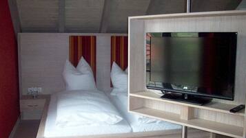 A bedroom with a bed, a TV on a stand, a nightstand, and a red wall.