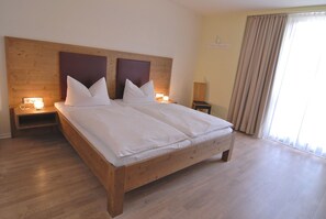 A large bed with two nightstands, wooden headboard, and a window with curtains. - RotHweinHotel (Wiesenbronn)