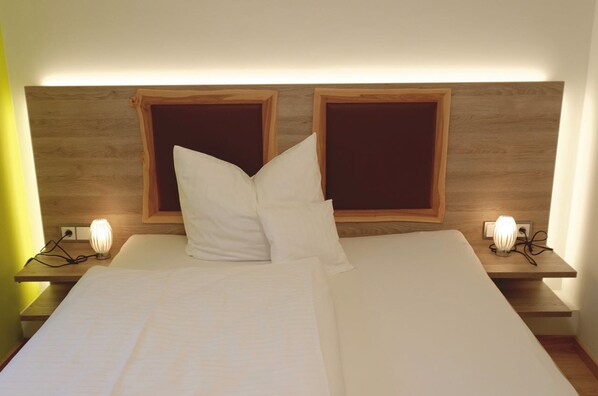 A neatly made bed with white linens, two bedside lamps, and a wooden headboard with a light fixture.