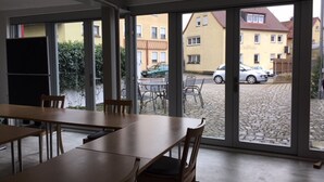 A dining area with large windows, a fire exit sign, and outdoor seating visible through the glass. - RotHweinHotel (Wiesenbronn)