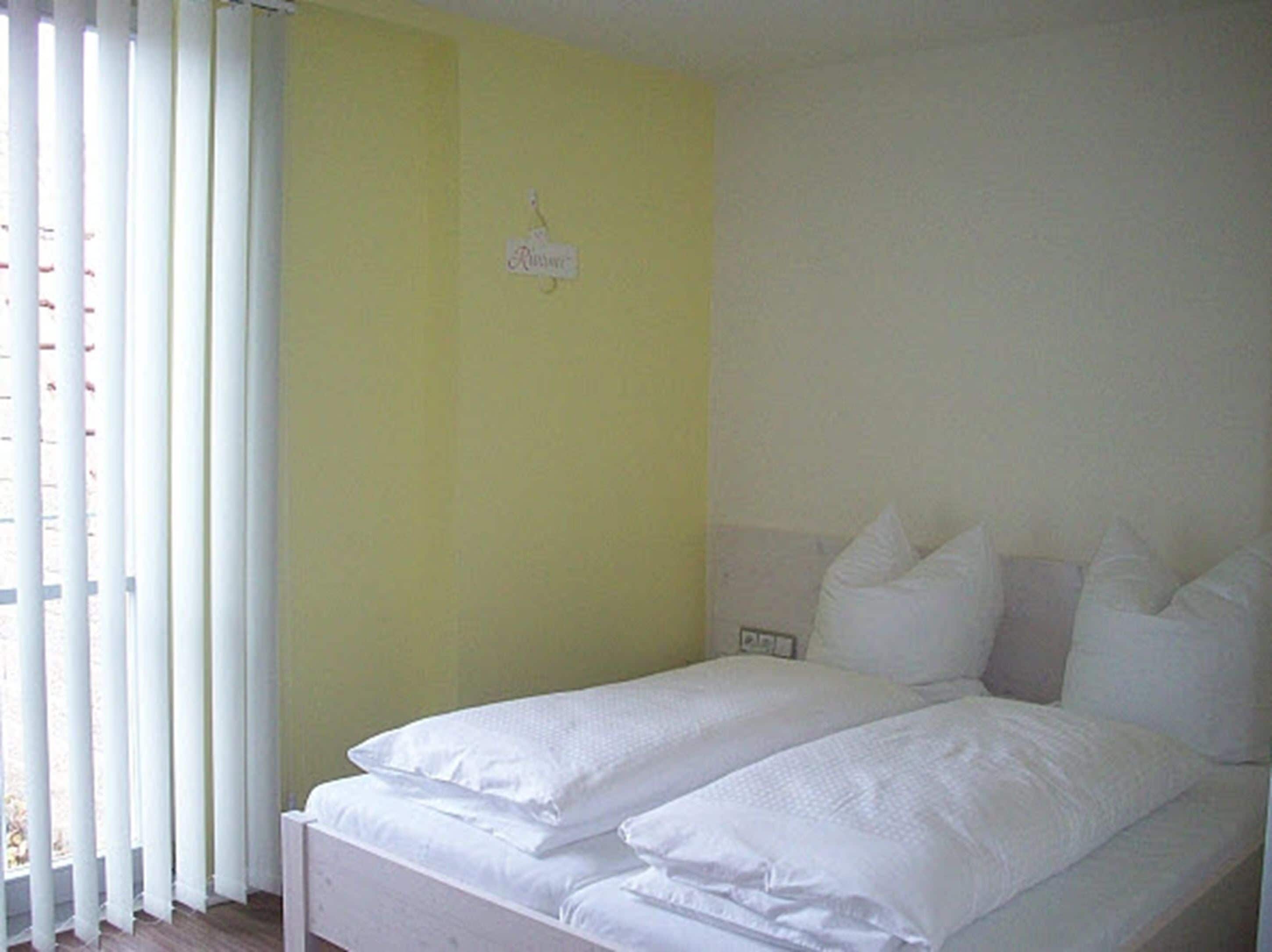 Ein Zimmer mit einem Bett, weißer Bettwäsche und einer gelben Wand.