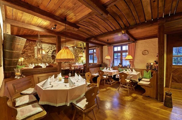 Un comedor rústico con mesas y bancos de madera, paredes de piedra e iluminación cálida.
