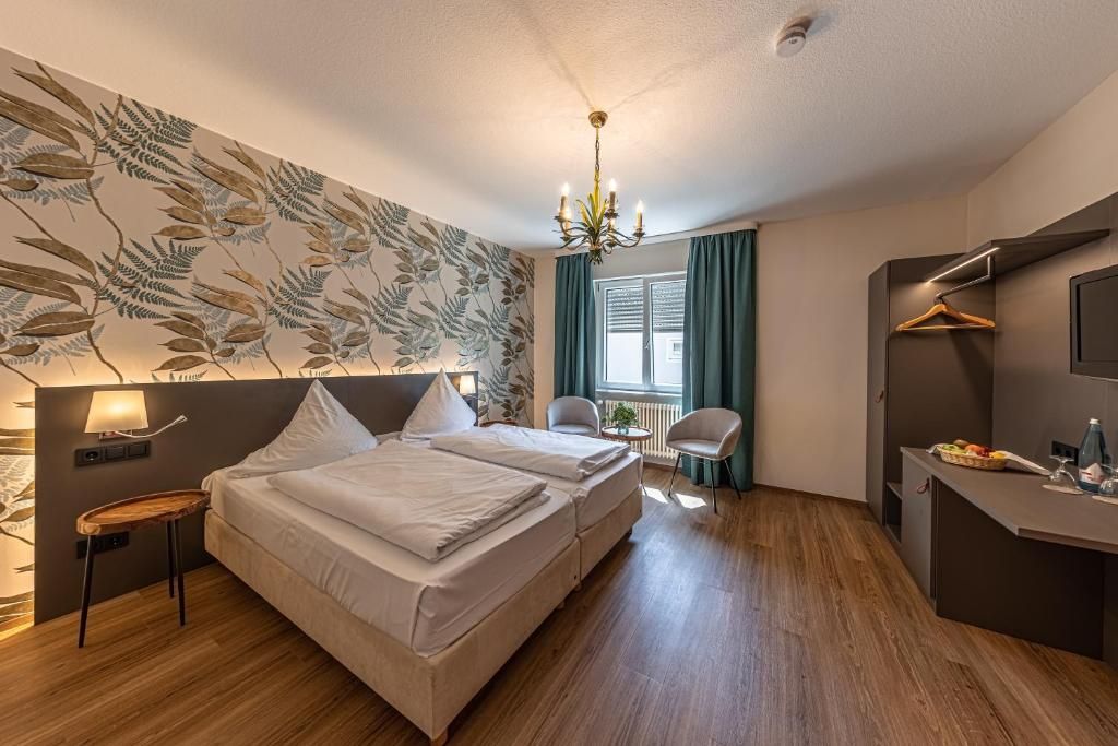Een hotelkamer met een bed, nachtkastje, lamp en een muur met een bladmotief.