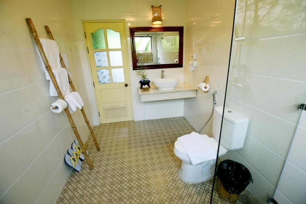 A bathroom with a toilet, sink, and mirror. There is a towel rack with towels and a pair of shoes on the floor.