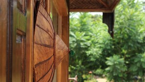 Eine Holztür mit traditionellem Design, einem grünen Quaste und Blick auf üppiges Grün im Hintergrund.