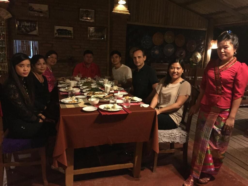 A group of people seated around a table with various dishes and glasses, in a room with brick walls and traditional decor.