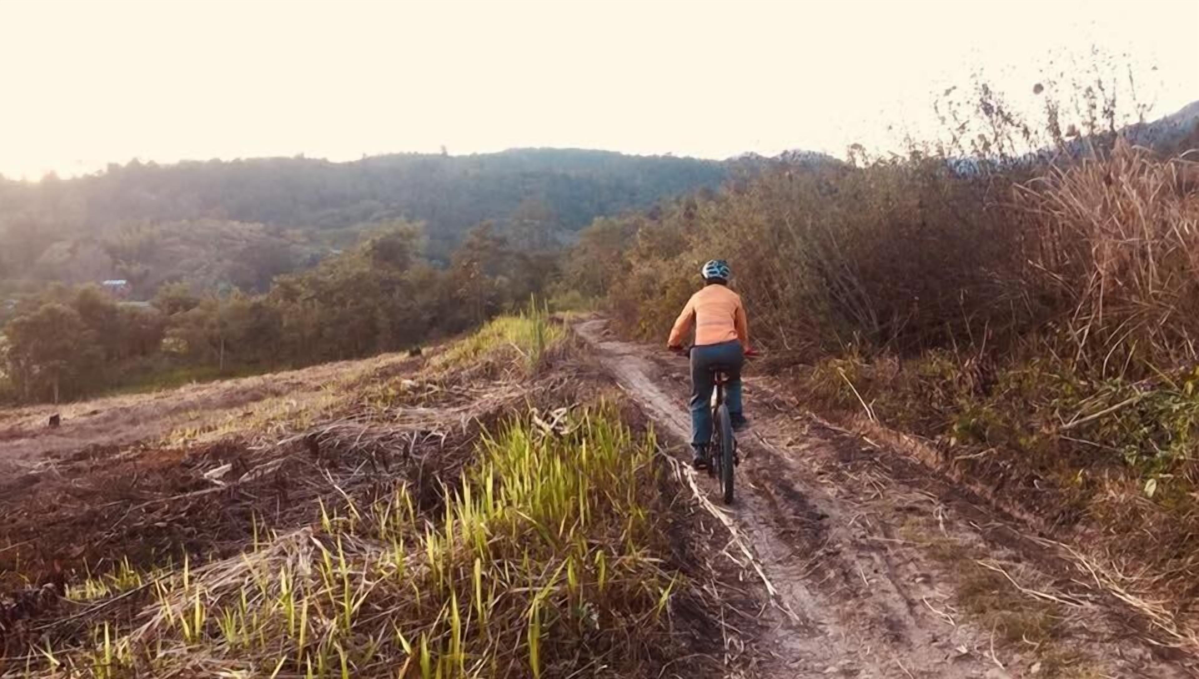A person riding a bicycle on a dirt path surrounded by vegetation and hills.